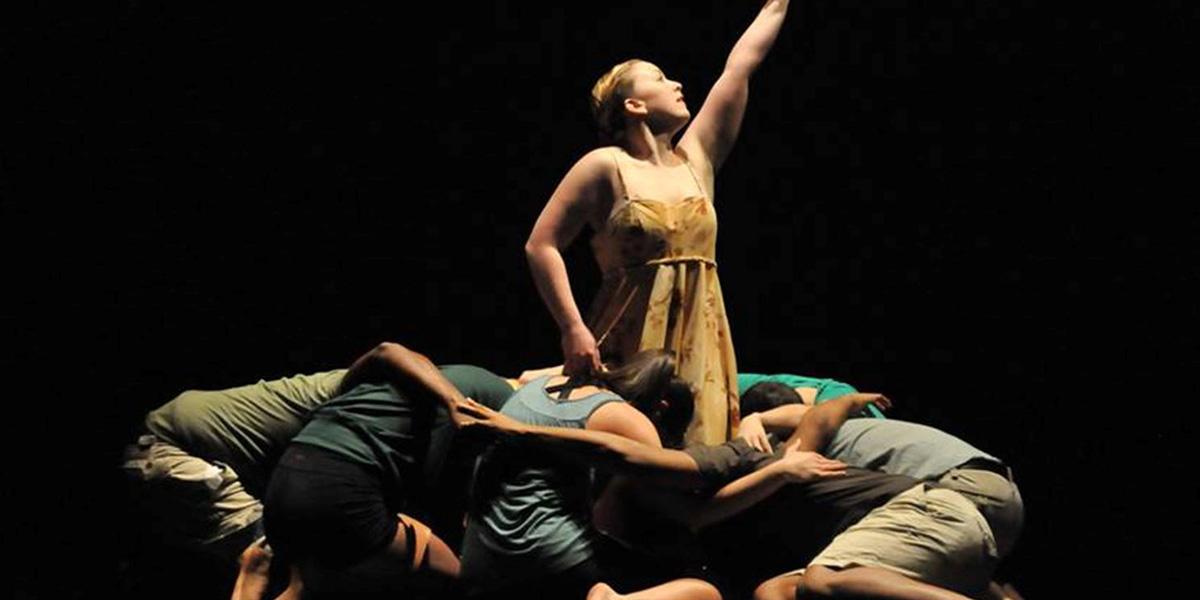 AACC dancers huddle around a single dancer on stage.